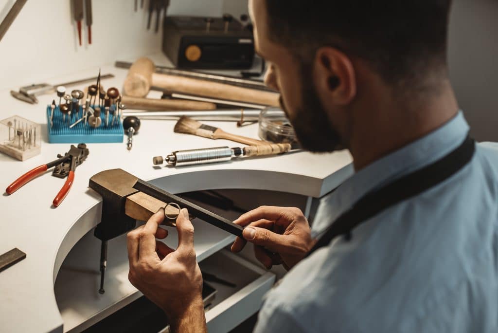 Delicate jewelry work. Close up of a male jeweler working and shaping an unfinished ring with a tool